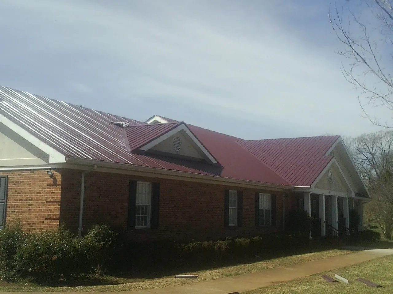 Red metal roof with gabled entries on a long brick building, from a Hail Damage Roof Repair job in White Oak